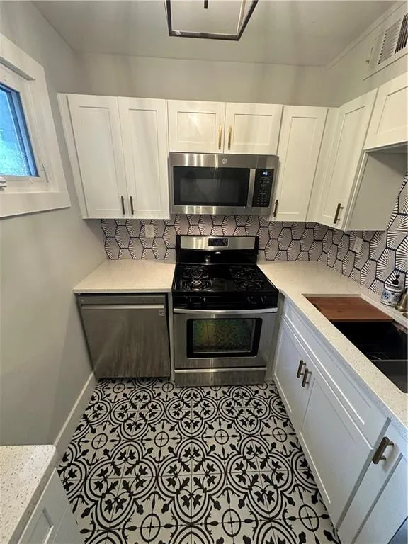 Kitchen with white cabinets, stainless steel appliances, light stone counters, and tasteful backsplash