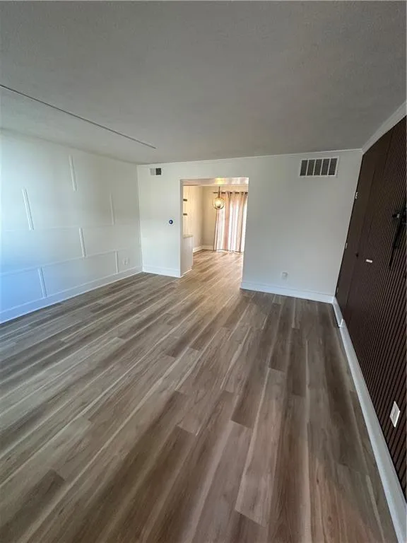 Unfurnished living room featuring wood finished floors, a textured ceiling, a chandelier, and a decorative wall