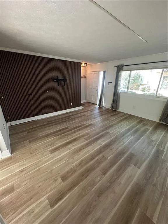 Unfurnished living room with light wood-style floors, a textured ceiling, and crown molding