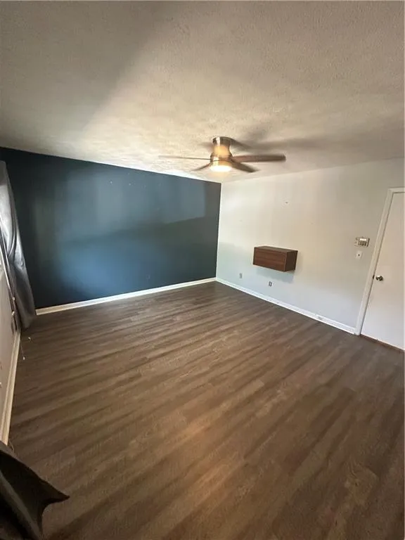 Unfurnished room with a textured ceiling, dark wood-style flooring, and ceiling fan