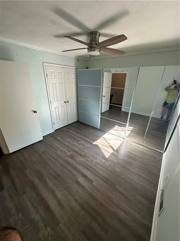 Unfurnished bedroom with dark wood-style flooring, a textured ceiling, ceiling fan, ornamental molding, and two closets