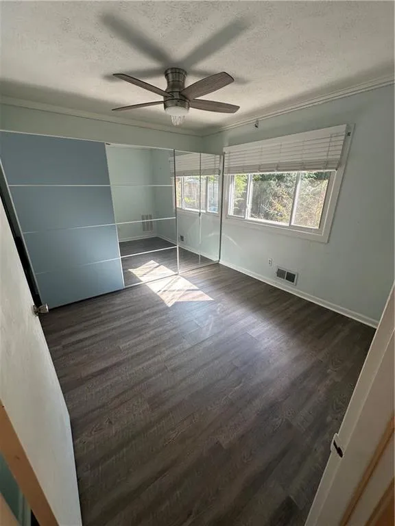 Unfurnished bedroom featuring dark wood-style floors, a textured ceiling, ornamental molding, and ceiling fan