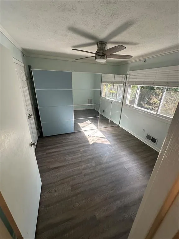 Unfurnished bedroom with a textured ceiling, dark wood-type flooring, ceiling fan, and ornamental molding