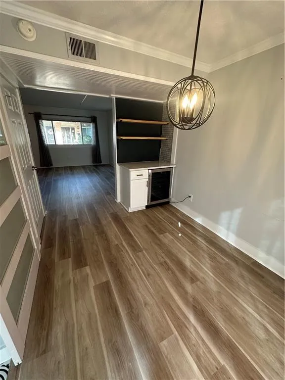 Unfurnished living room with dark wood-style flooring, ornamental molding, beverage cooler, a chandelier, and a textured ceiling