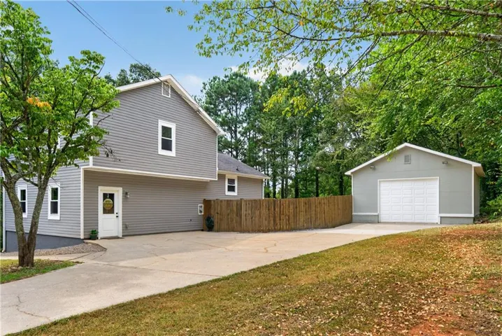 Gray siding exterior, white trim details, white entry door, detached garage with white garage door, and a privacy fence