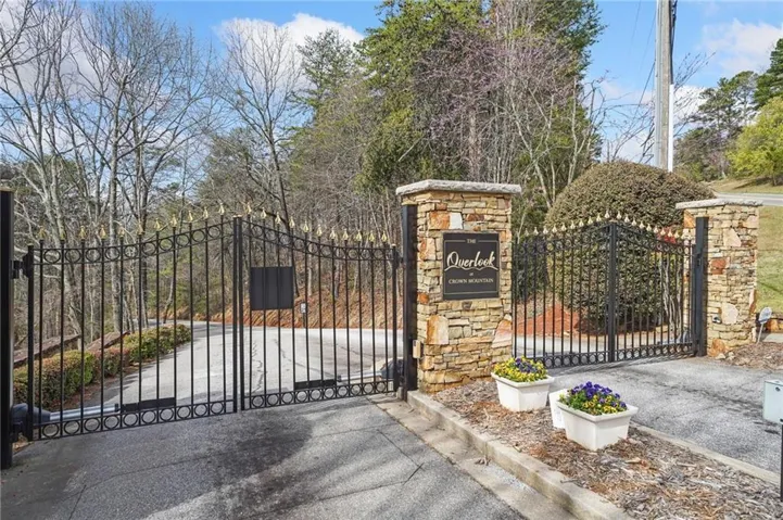 Wrought iron entry gate with decorative gold-finished finials, flanked by stone-clad pillars, featuring a carved stone sign