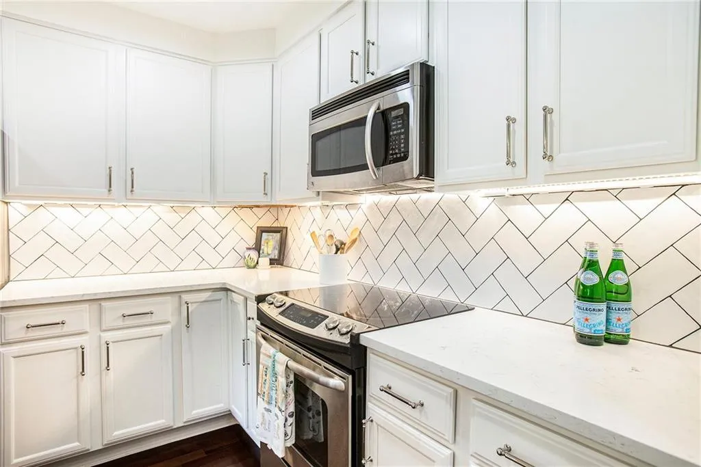 Kitchen featuring white cabinetry, light stone counters, dark hardwood / wood-style floors, appliances with stainless steel finishes, and decorative backsplash
