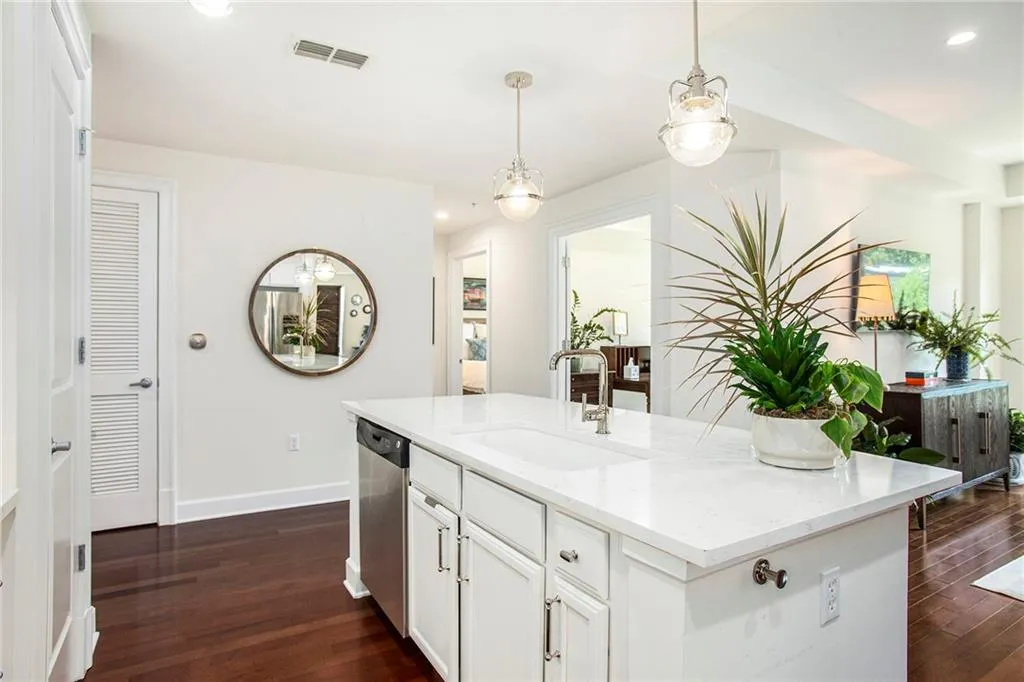 Kitchen with a center island with sink, sink, hanging light fixtures, stainless steel dishwasher, and dark wood-type flooring