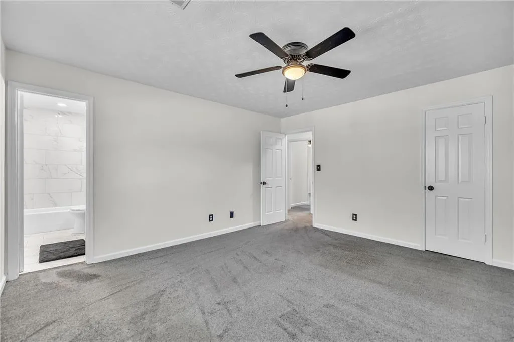 Unfurnished bedroom featuring ensuite bath, a textured ceiling, a ceiling fan, and carpet floors