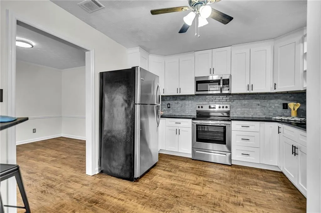 Kitchen with stainless steel appliances, dark wood-style flooring, decorative backsplash, white cabinetry, and ceiling fan