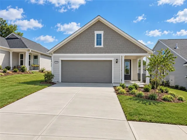 Contemporary exterior featuring a covered entry, attached garage, shingle siding, and established landscaping