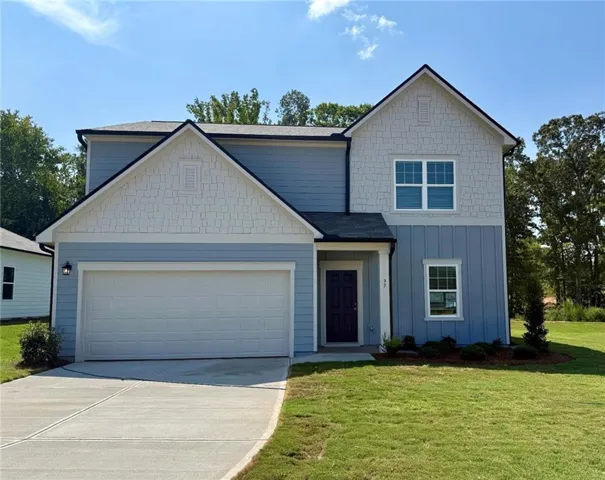 Two-story residential structure featuring multiple siding textures, an attached garage, a dark entry door, and a concrete driveway
