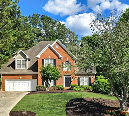 Brick exterior with a gabled roofline, featuring a two-car garage, manicured front lawn, and established landscaping