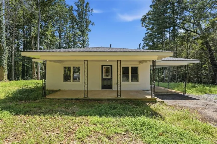 Charming cottage-style home featuring a cream exterior with dark trim, covered front porch with metal railings, and expansive metal carport