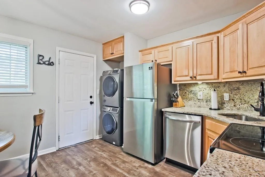 Kitchen with light stone counters, light brown cabinets, stainless steel appliances, backsplash, and light wood finished floors