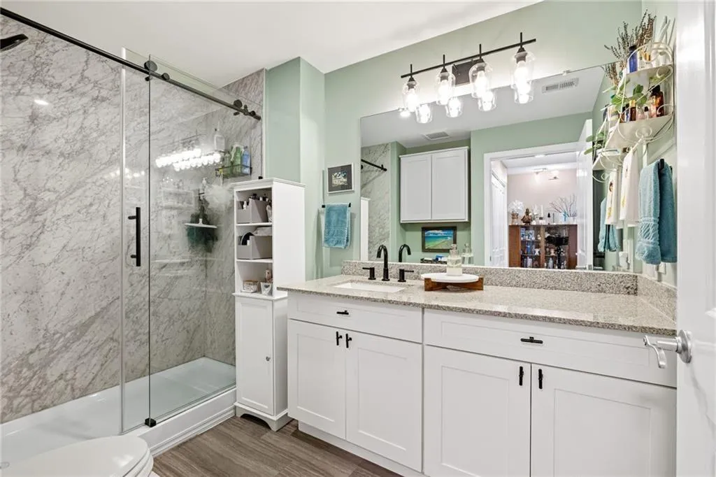 Shower with sliding glass door, grey stone-finish tile surround, and built-in shelving