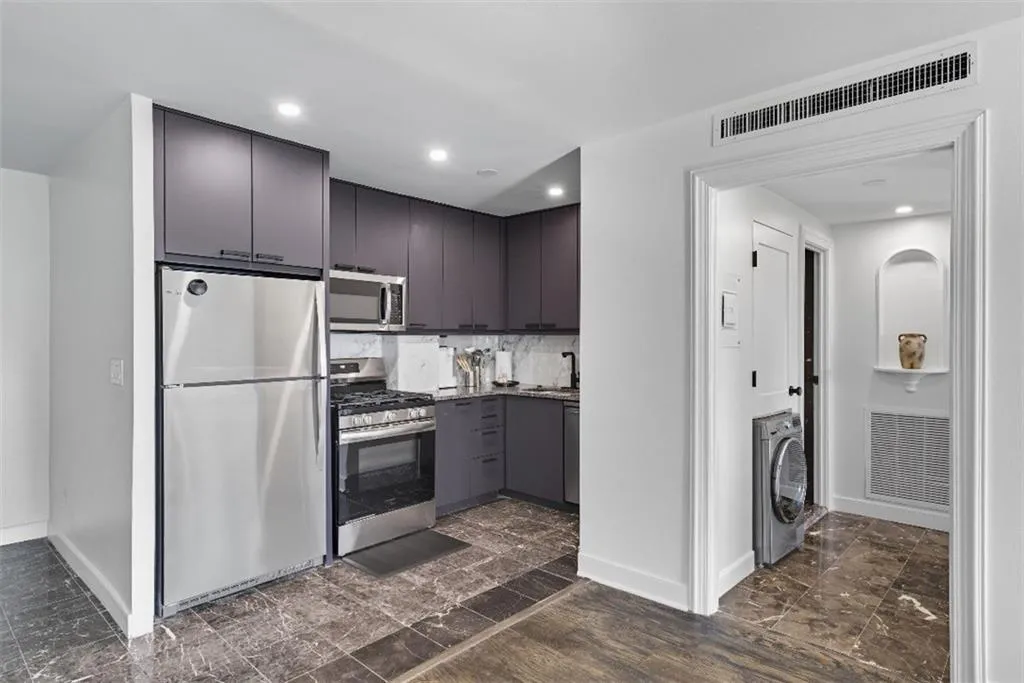 Kitchen featuring stainless steel appliances, washer / clothes dryer, modern cabinets, recessed lighting, and light stone counters