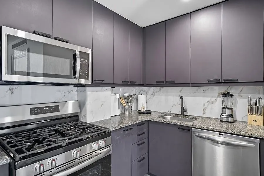 Kitchen featuring appliances with stainless steel finishes, light stone counters, gray cabinets, backsplash, and modern cabinets