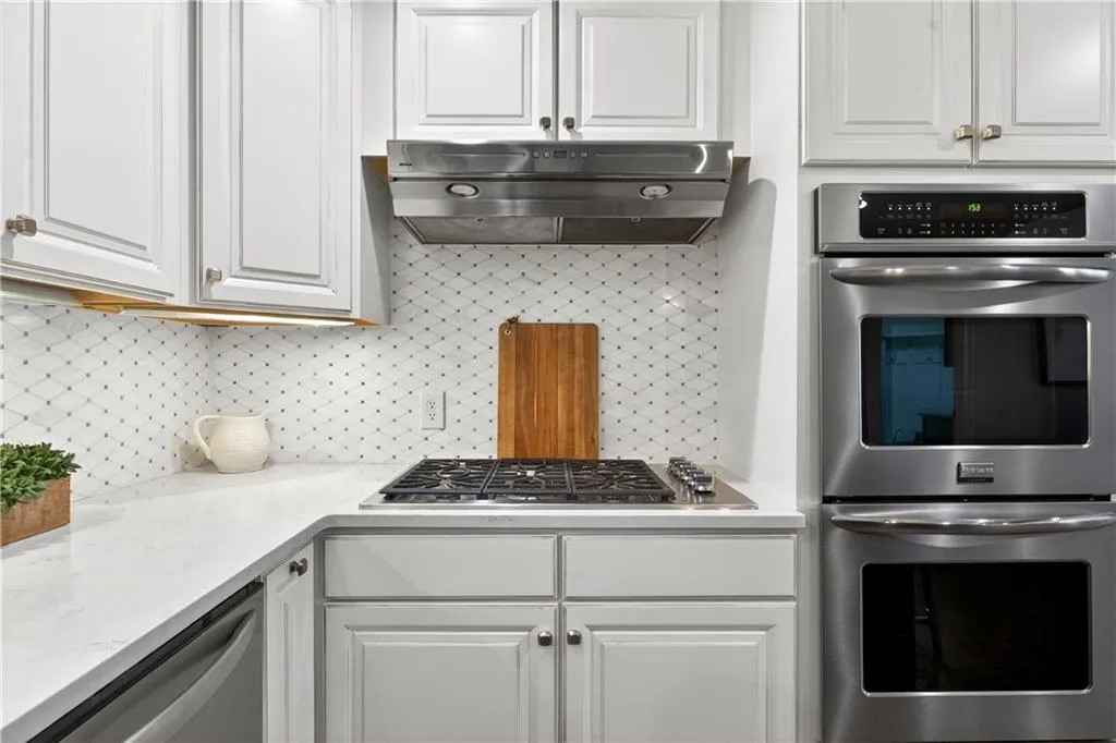 Kitchen with stainless steel appliances, white cabinetry, light stone countertops, and backsplash