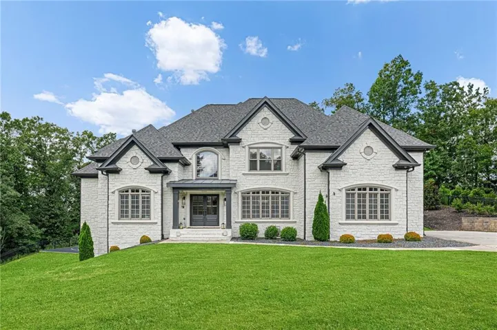 White stone exterior, dark gray shingled roof, arched and rectangular windows, dark gray trim, and a manicured lawn