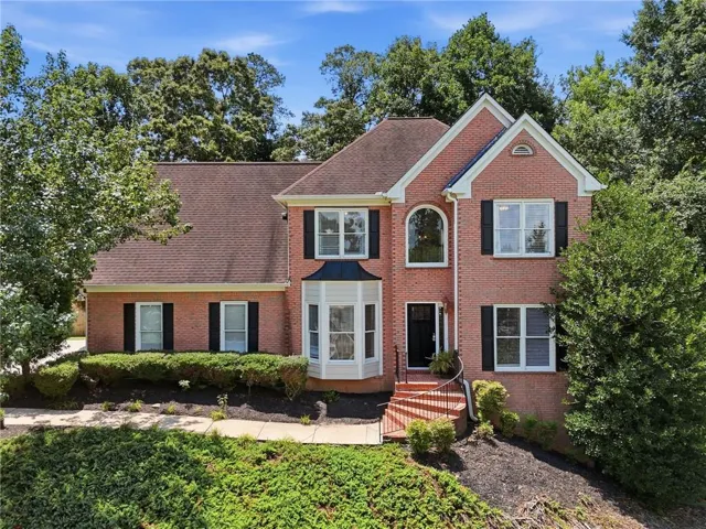 Traditional brick-clad home featuring a prominent bay window, arched entry window, and black louvered shutters