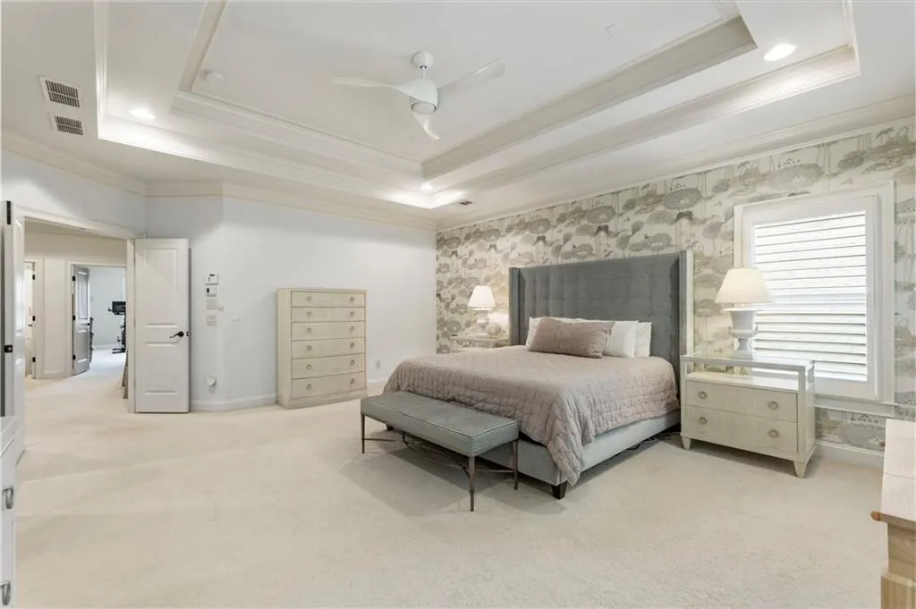 Bedroom featuring a raised ceiling, light colored carpet, crown molding, ceiling fan, and wallpapered walls