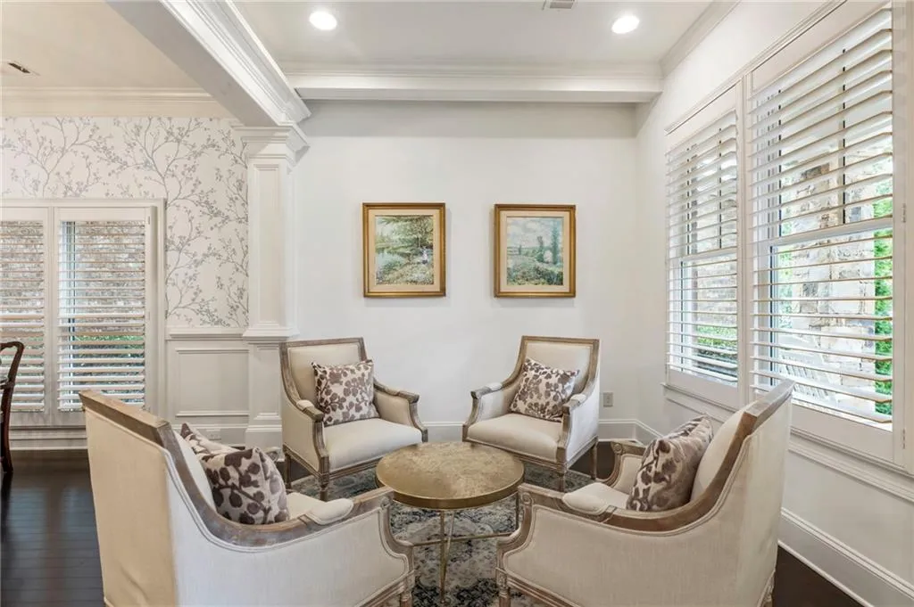Living area featuring ornamental molding, wainscoting, a decorative wall, dark wood-style floors, and ornate columns