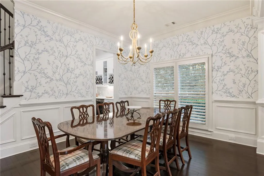 Dining area with wallpapered walls, a decorative wall, crown molding, dark wood-type flooring, and a chandelier