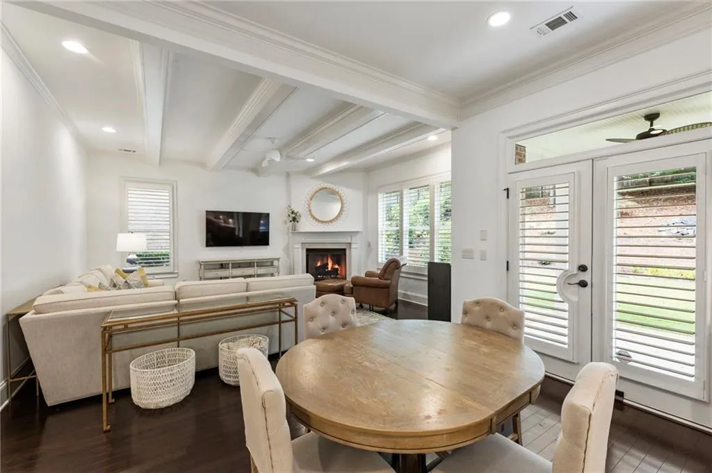 Dining room featuring beamed ceiling, dark wood finished floors, a warm lit fireplace, healthy amount of natural light, and a ceiling fan
