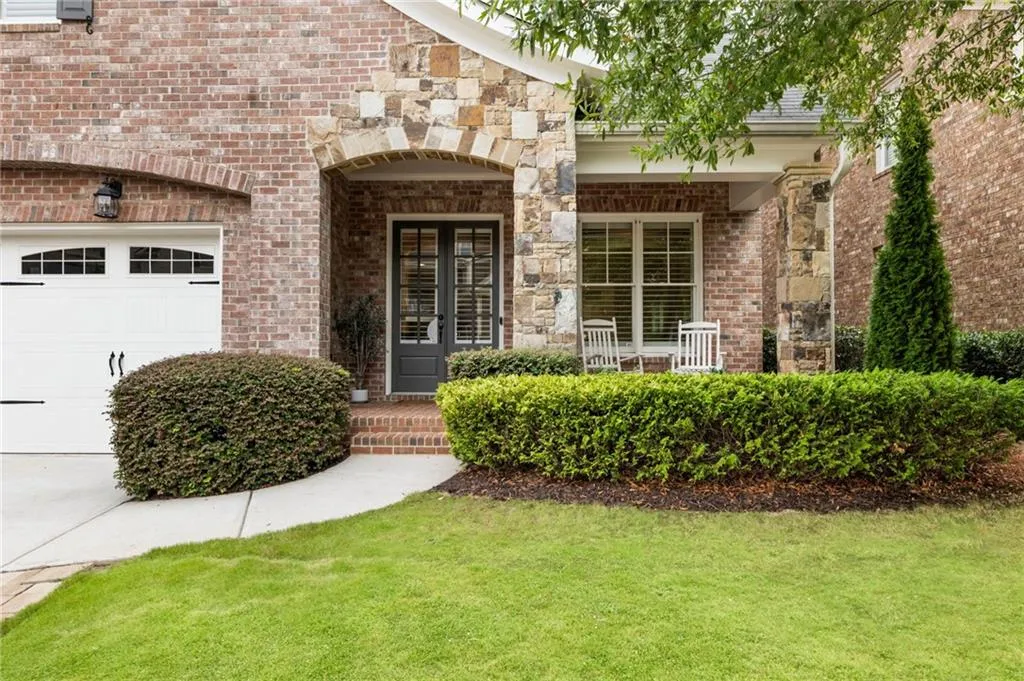 Entrance to property featuring covered porch, brick siding, a garage, and a yard