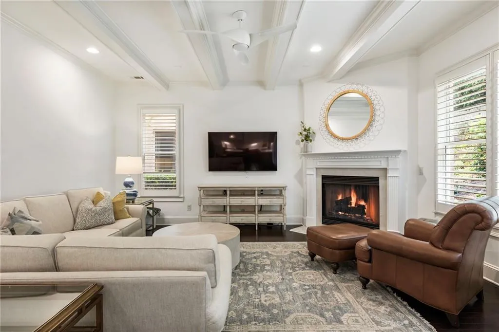 Living room featuring beamed ceiling, a warm lit fireplace, recessed lighting, wood finished floors, and crown molding