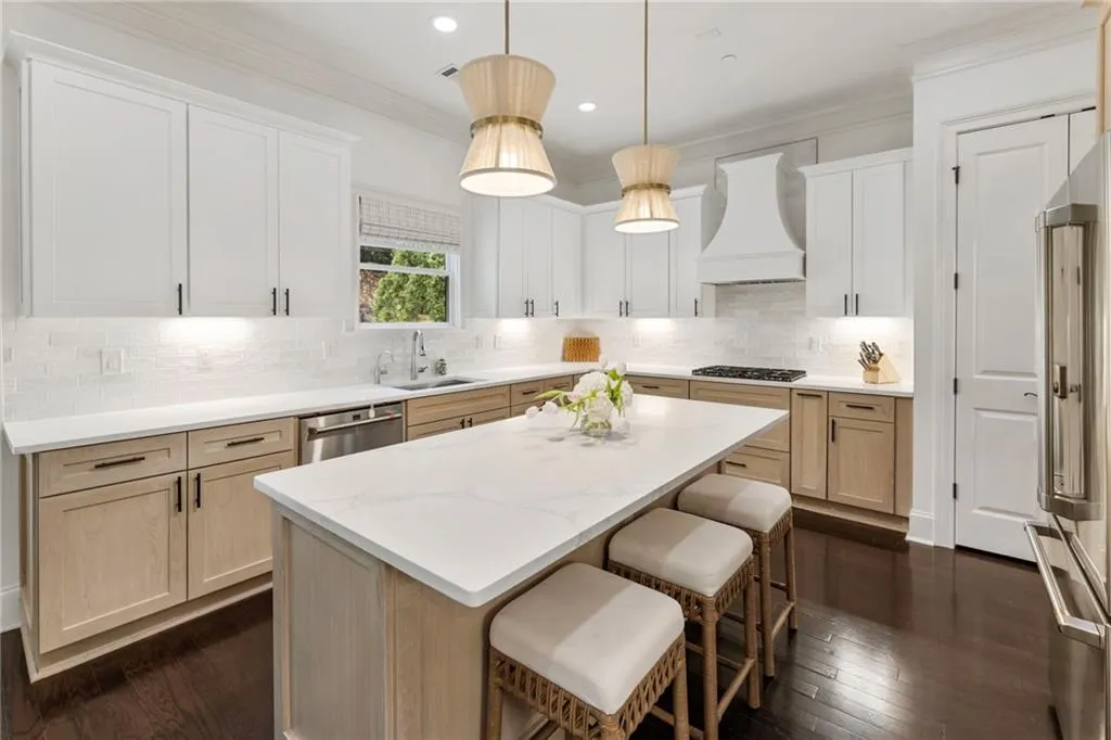 Kitchen with light brown cabinets, crown molding, decorative light fixtures, dark wood-style flooring, and appliances with stainless steel finishes