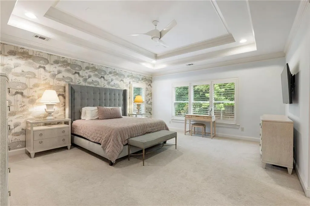 Carpeted bedroom with a raised ceiling, ornamental molding, wallpapered walls, and a ceiling fan