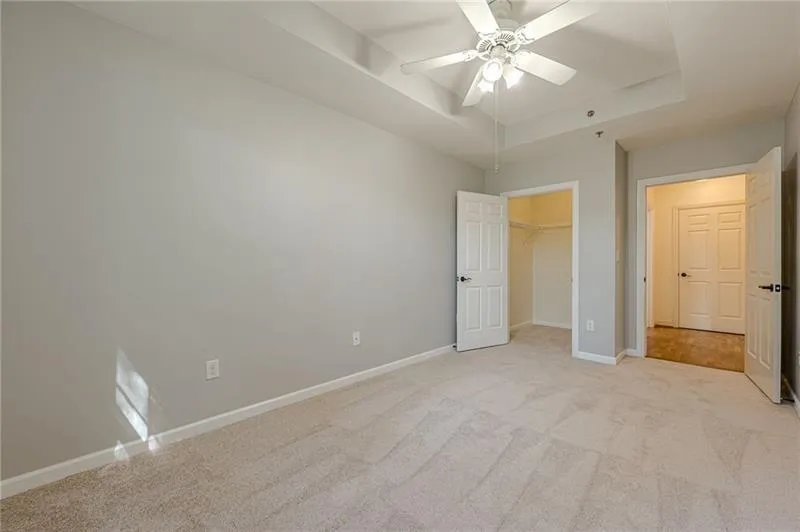 Unfurnished bedroom featuring a raised ceiling, light colored carpet, a spacious closet, and a ceiling fan