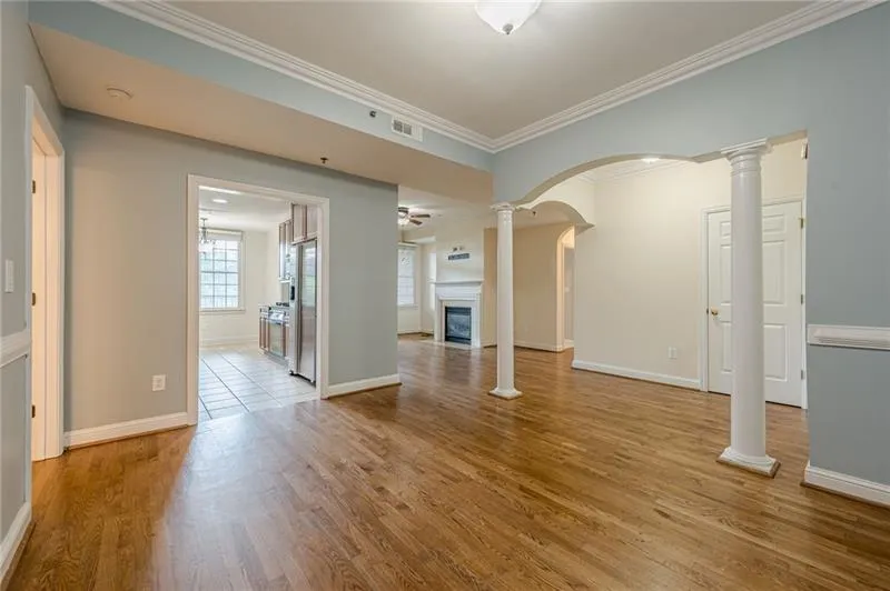 Unfurnished living room with ornate columns, ornamental molding, arched walkways, a glass covered fireplace, and light wood finished floors