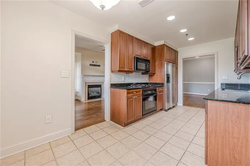 Kitchen featuring backsplash, dark stone countertops, brown cabinets, black appliances, and light tile patterned flooring