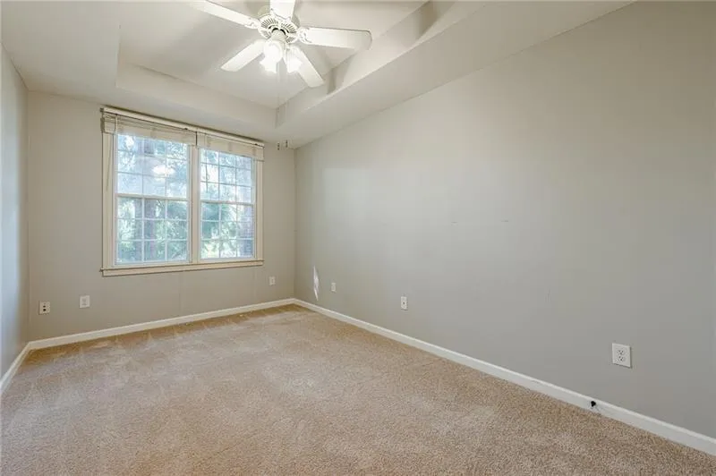 Empty room featuring a tray ceiling, light colored carpet, and a ceiling fan