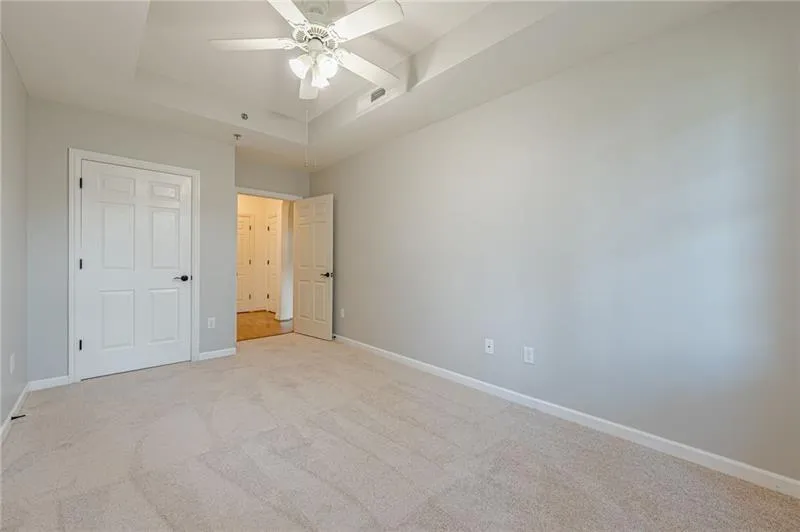 Unfurnished bedroom featuring light colored carpet, a tray ceiling, ceiling fan, and a closet
