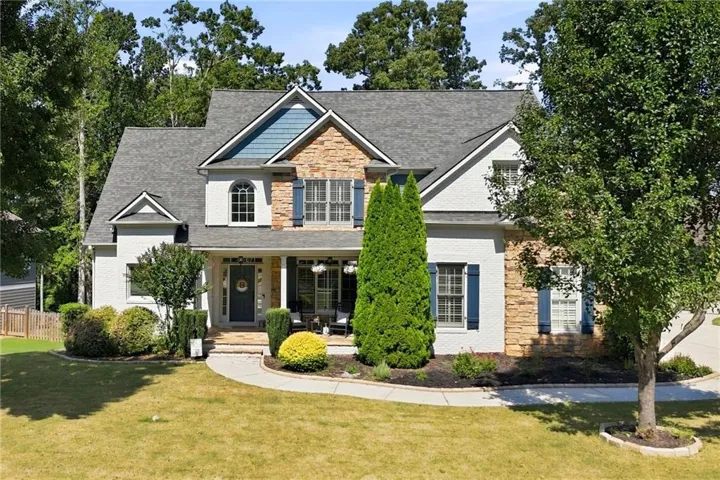 Two-story residence featuring a mixed-material exterior, a covered front porch, a gabled roofline, a paved walkway, and mature landscaping