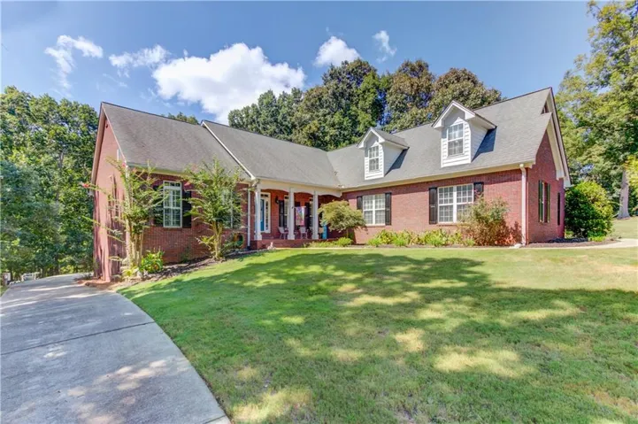 Brick exterior with dormer windows, a covered front porch, a well-maintained lawn, and a paved driveway
