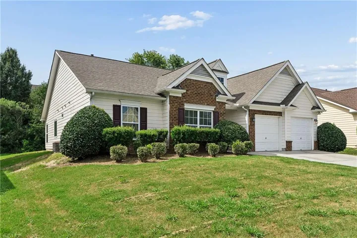 White siding exterior with brick accents, two-car garage, and mature landscaping