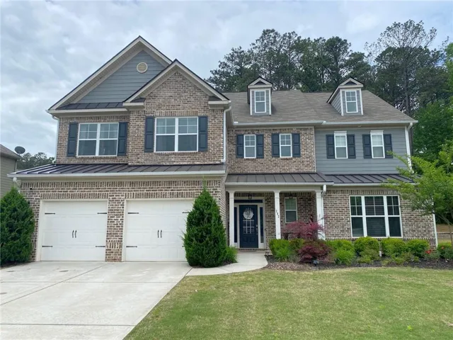 Multi-story residence featuring a brick and siding exterior, a two-car garage with white doors, and a covered front porch with white columns