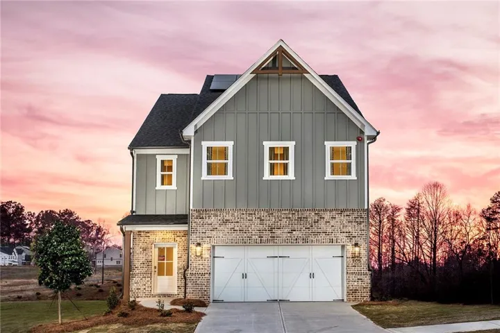 View of front of house with board and batten siding, an attached garage, concrete driveway, brick siding, and a shingled roof