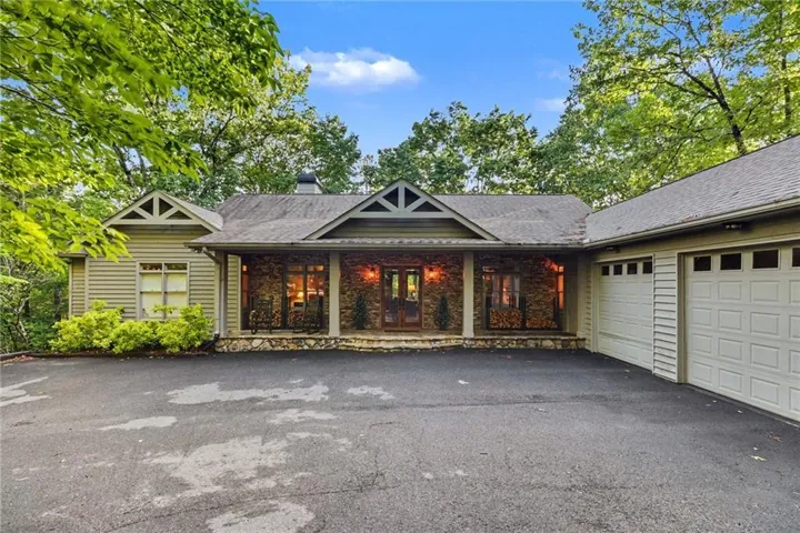 Stone and siding exterior featuring a covered front porch with stone pillars, a prominent gable roofline, an attached two-car garage, and a paved driveway