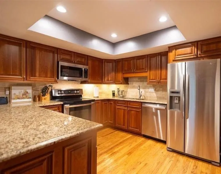 Kitchen with appliances with stainless steel finishes, light stone counters, a raised ceiling, and sink