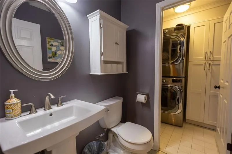 Bathroom with toilet, tile patterned flooring, stacked washer / drying machine, and sink