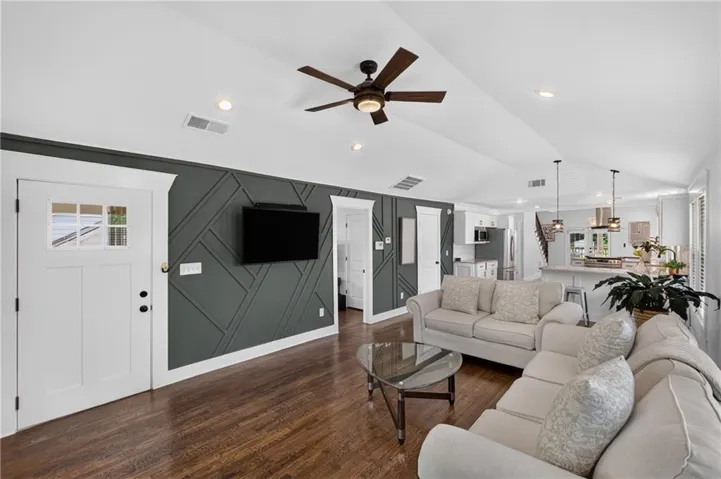 Spacious living area featuring vaulted ceilings, wood-finish flooring, a decorative accent wall, recessed lighting, and a ceiling fan