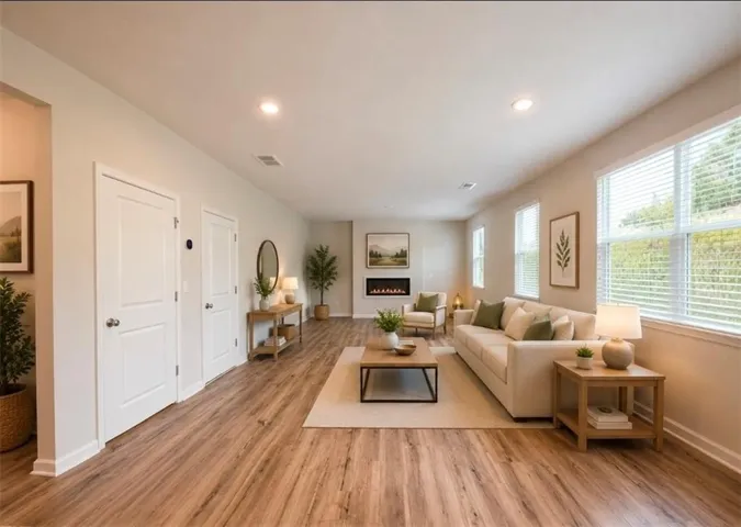 Spacious living area featuring wood-finish flooring, recessed lighting, multiple windows with blinds, a built-in electric fireplace, and two white panel doors