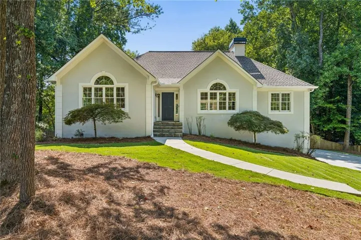 Stucco exterior with a shingled roof, arched transom windows, dark entry door, and stone steps