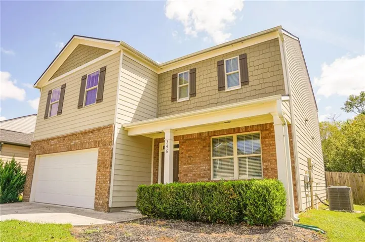 Two-story residence featuring a brick and siding exterior, an integrated garage, covered front entry, and mature front landscaping